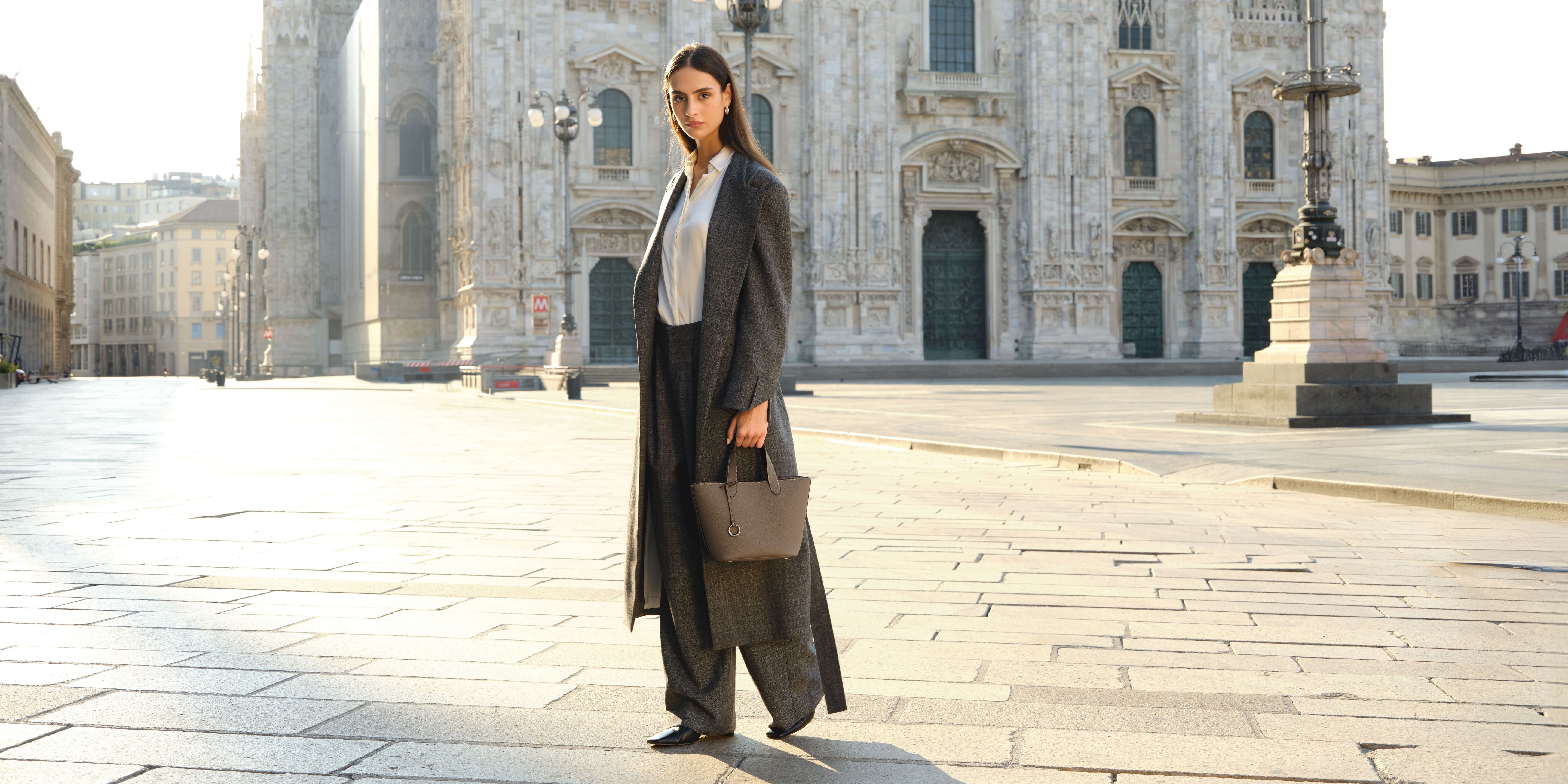 Elegant woman in a coat walking Milan city center with a small brown premium leather tote, business-ready.